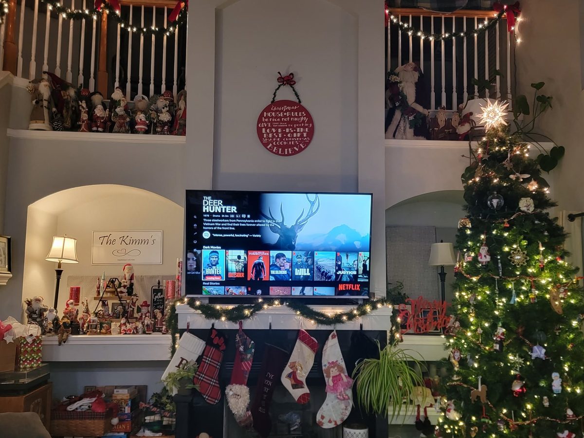 A living room decorated for Christmas: a lit tree, garland on the mantel, stockings, and a Santa collection along the upper ledges