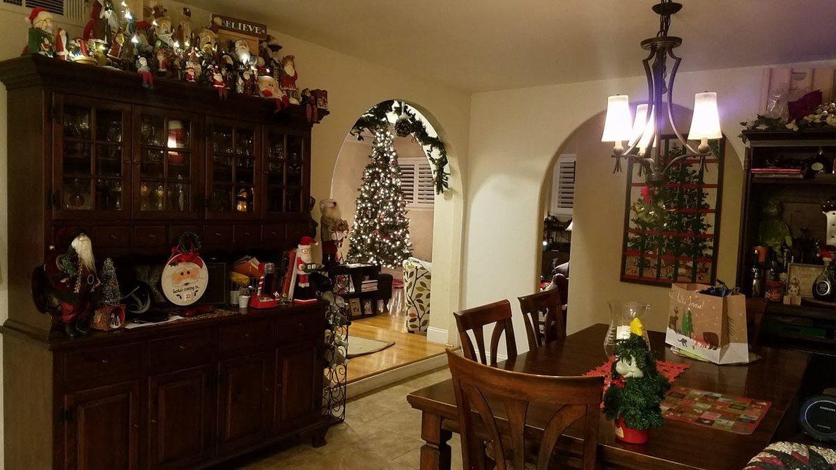 A dining room at Christmas: a collection of Santa figures lined up on top of a wooden hutch, more Santas on the counter, and a lit tree through the archway