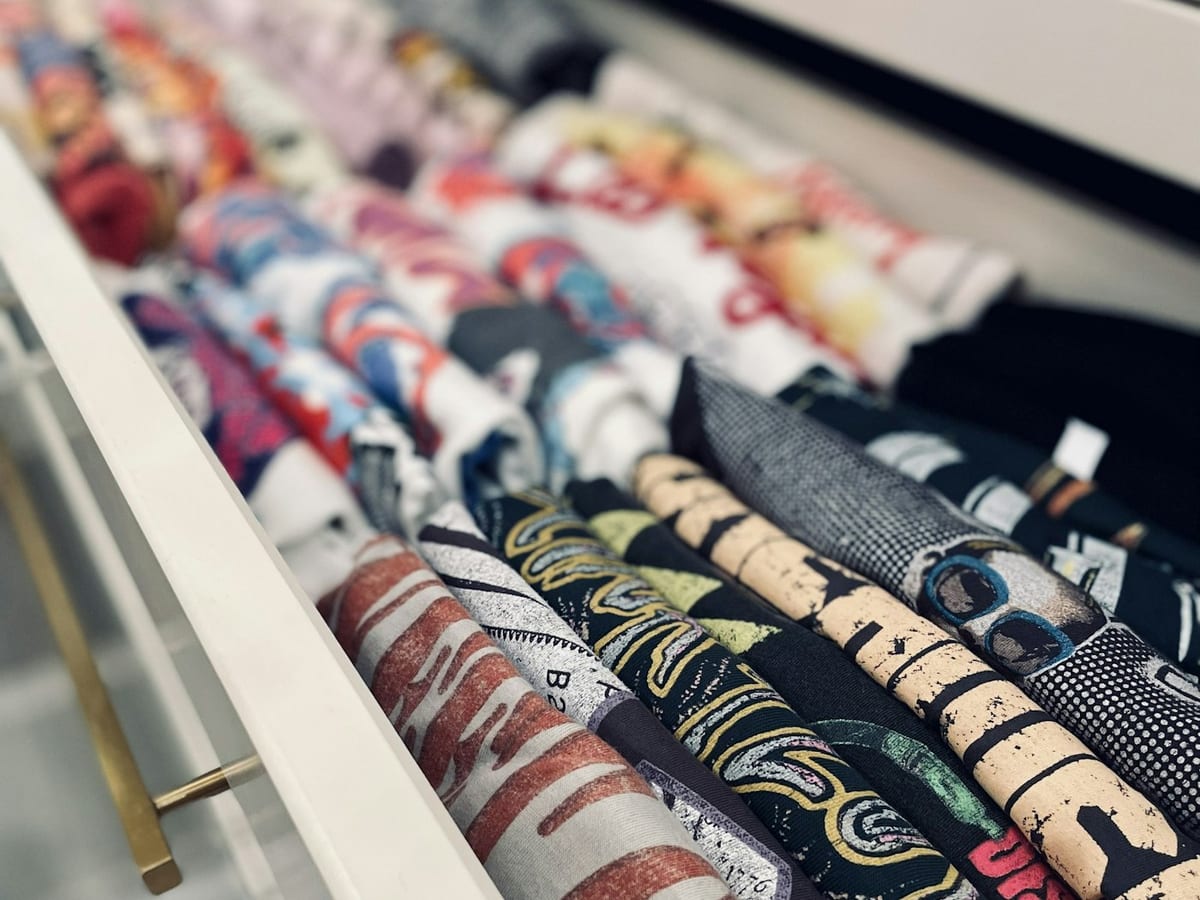 An open dresser drawer of graphic T-shirts rolled and lined up in rows, every one visible at a glance